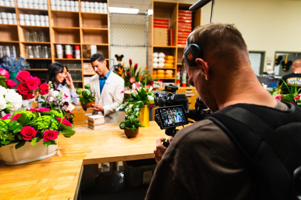 A camera operator filming people working with flowers on location
